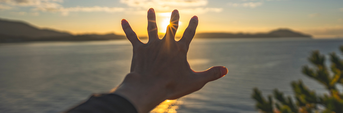 朝日に手を伸ばす男性